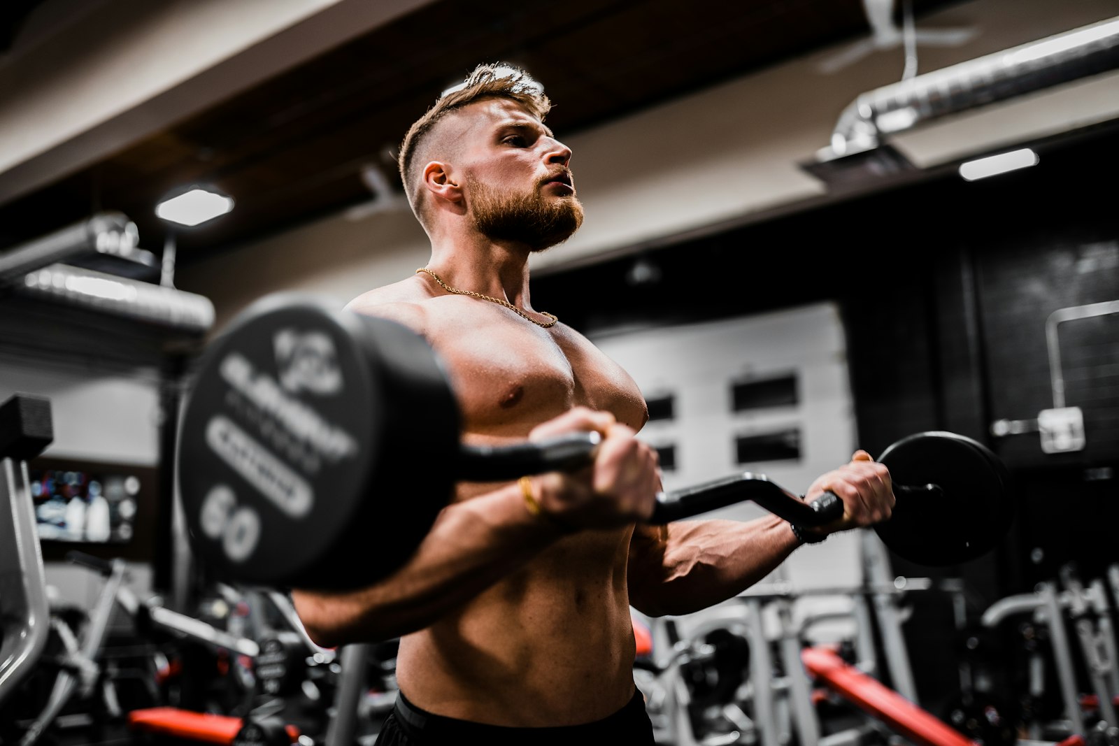 Un sportif en pleine série de curl à la barre, en salle de musculation